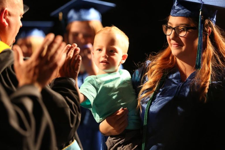 Graduate Walking With diploma while holding her child